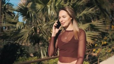 Şehir parkında yürürken güzel bir kızın mutlu bir şekilde akıllı telefondan konuştuğunu gösteren bir fotoğraf.