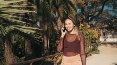 Renkli güzel sarışın kız. Arka planda avuç içleri olan akıllı telefondan mutlu bir şekilde konuşuyor. Mavi gözlü genç bir kadın telefonda konuşuyor.