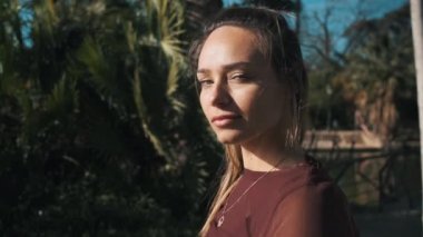 Park boyunca göl kenarında yürürken güneşin altında kameraya şehvetle bakan güzel bir kızın portresi. Çekici, rüya gibi, renkli bluzlu kız.