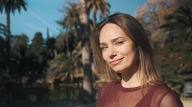 Parkta poz verirken mutlu ve cilveli bir şekilde gülümseyen güzel bir kız. Çekici, baştan çıkarıcı, mavi gözlü, kameraya bakan sarışın kadın.