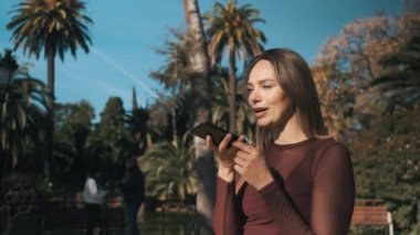 Güzel, neşeli bir kız telefonuyla mutlu bir şekilde konuşuyor. Parkta gülüyor ve gülüyor. Mutlu çekici kız telefonda konuşuyor.