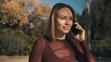 Çekici, neşeli, mutlu bir şekilde gülen bir kız. Şehir parkında erkek arkadaşıyla telefonda konuşuyor. Güzel sarışın kız telefonda flört ediyor. 