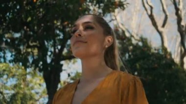 Genç ve güzel bir kadın parkta mandalina bahçesinde mutlu bir şekilde yürüyor. Çekici, mutlu Latin bir kızın portresinin izini sürüyorum.