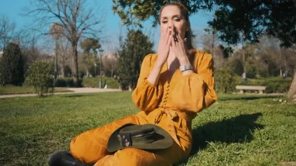 Parktaki Çimlerde Oturan Kameraya Mutlu Bir Şekilde Öpücükler Yollayan Genç — Stok video