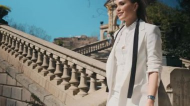 Klasik beyaz takım elbiseli genç ve güzel bir kadın eski şehir parkında merdivenlerden iniyor.