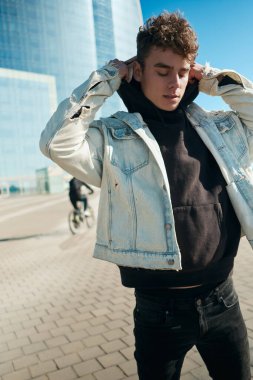 Şehir caddesinde yürürken kapüşonlu kot ceket giyen şık bir genç.