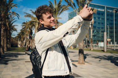 Sırt çantalı yakışıklı adam şehrin caddesinde akıllı telefondan fotoğraf çekiyor. Genç turist yeni şehri keşfediyor.