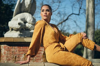 Turuncu tulumlu, dışarıda kameraya güvenle poz veren genç ve güzel bir kadın.