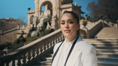 Klasik beyaz takım elbiseli muhteşem bir kadın eski şehir parkında merdivenlerde dikiliyor ve kameraya bakıyor.