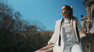 Klasik takım elbiseli güzel bir kadın kendinden emin bir şekilde parktaki merdivenlerde eski mimariyle poz veriyor.