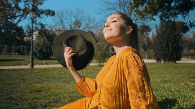 Parktaki çimlerin üzerinde rüyasında dinlenen parlak turuncu tulumlu genç bir kadın. Güneşin altında poz veren güzel bir model.