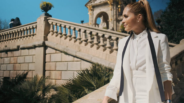 Young gorgeous woman in classic white suit confidently walking down the stairs in old city park