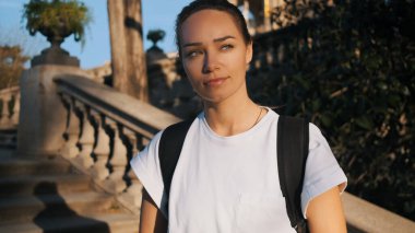 Sırt çantalı güzel bir kızın portresi kendinden emin bir şekilde dışarı bakıyor. Şehir merkezindeki merdivenlerde dinlenen çekici, sportif genç bir kadın.