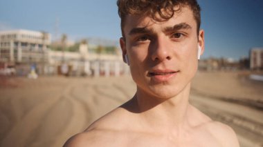 Yaklaş yakışıklı sporcu. Şehir plajında egzersiz yaparken kameraya özgüvenle bakıyor.