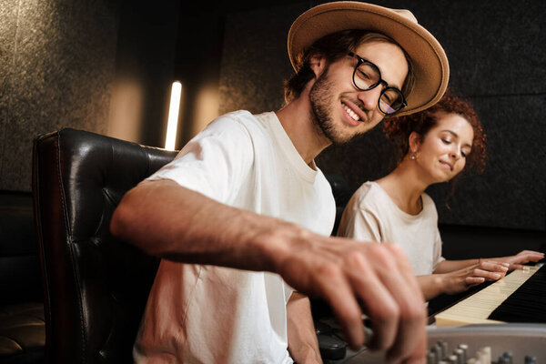 Young stylish people creating music in modern sound recording studio. Attractive musicians happily working in studio