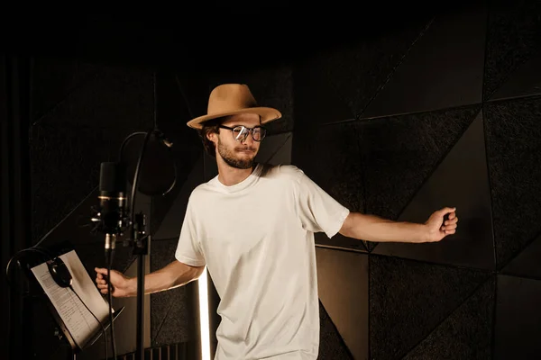 Attractive stylish musician dancing while recording new song in modern sound studio. Young male singer singing in studio