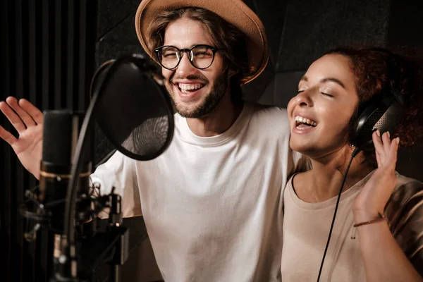 Portrait of young attractive man and woman happily singing together in modern sound recording studio