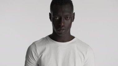 Beyaz tişörtlü ciddi bir Afro-Amerikan adamın portresi gri arkaplandan kameraya agresif bir şekilde bakıyor. Kızgın ifade