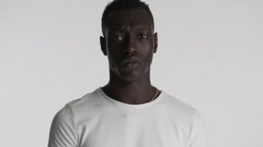 Genç üzgün Afro-Amerikalı beyaz tişörtlü adam gri arka plandan kameraya bakıyor. Stresli ifade