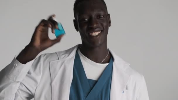 年轻迷人 快乐的非洲裔美国男医生 高兴地将消毒液瓶放在灰色的背景上 — 图库视频影像
