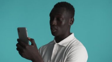 Genç, çekici, Afro-Amerikan bir adam akıllı telefondan renkli bir geçmişle görüntülü sohbet yapıyor. Elveda jest