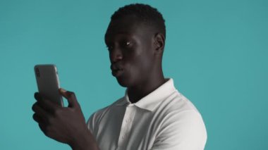 Çekici, kendine güvenen Afro-Amerikan adam renkli arka plan üzerinden akıllı telefondan arkadaşlarıyla görüntülü konuşma yapıyor.