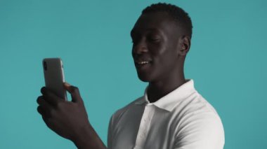 Akıllı telefonu kullanan çekici, gülümseyen Afro-Amerikan adam renkli arka plan üzerinden video konuşmalarında mutlu bir şekilde selam veriyor. Selamlama ifadesi