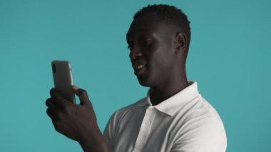 Akıllı telefonu kullanan çekici, gülümseyen Afro-Amerikan adam renkli arka planda arkadaşlarıyla görüntülü sohbette mutlu bir şekilde konuşuyor.