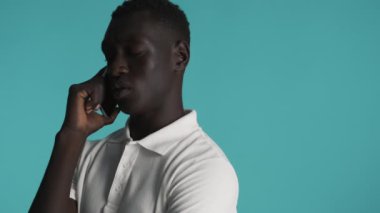Genç, üzgün, Afro-Amerikan bir adam akıllı telefondan renkli bir arkaplanda konuşuyor. İfadeyi kapat