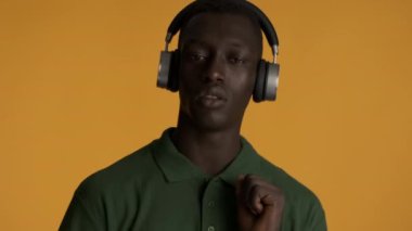 Yakışıklı Afrikalı Amerikalı kulaklıkla müzik dinleyen turuncu arka planda kamerada güvenle dans eden adam.