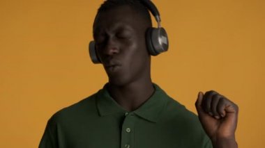 Kulaklıklı genç, şık Afrikalı Amerikalı adam renkli arka planda şarkı söyleyip dans ediyor.