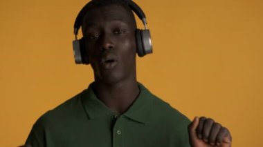 Yakışıklı Afro-Amerikalı kulaklıklı adam. Renkli arka planda duygusal olarak şarkı söyleyip dans ediyor.