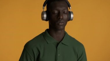 Çekici stil sahibi kulaklıklı Afro-Amerikan adam gözlerini kapatıp renkli arka planda dans ediyor. Dinleyen müzik ifadesi