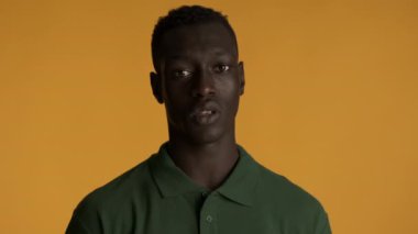 Genç, afro-amerikan bir adam korkakça arkasını dönüyor ve renkli arka planda duruyor. İfadeyi izlemek istemiyorum.