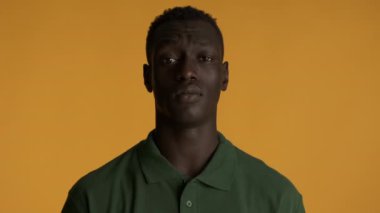 Genç, ciddi, Afro-Amerikan bir adam renkli arka planda kameraya poz veriyor. Yorgun ifade