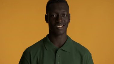 Çekici gülümseyen Afro-Amerikan adam kendine güvenerek renkli arka planda kameraya bakıyor.