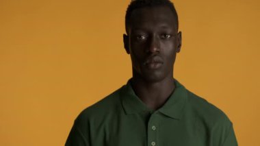 Genç, ciddi, Afro-Amerikan bir adam, saldırgan bir şekilde renkli arka planda kameraya bakıyor. Yüz ifadesi