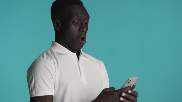 Młody Zdumiony Afroamerykanin Używający Smartfona Niebieskim Tle Wow Ekspresja — Wideo stockowe