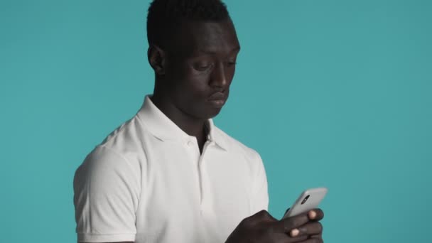 Молодой Привлекательный Афроамериканец Интенсивно Использует Смартфон Синем Фоне Удивлённое Выражение — стоковое видео