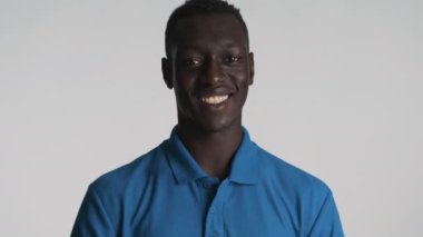 Yakışıklı, gülümseyen Afrikalı Amerikalı adam gri arka planda başparmak işareti yapıyor. İfade gibi