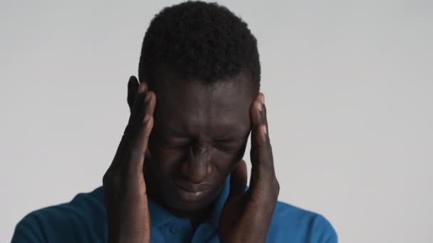 若い悲しいアフリカ系アメリカ人の男性が灰色の背景に頭痛を感じる指で寺院をマッサージ 痛みの表現 — ストック動画