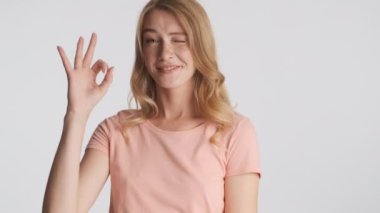 Genç neşeli sarışın kadın mutlu bir şekilde göz kırparak iyi niyet gösteriyor ve gri arka planda kameraya gülüyor. İfade etrafında dolaşmak