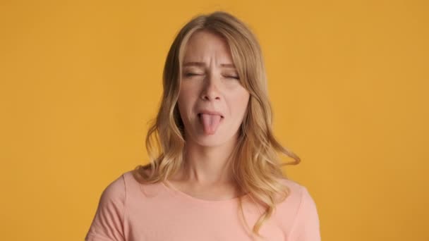 若い面白いブロンドの女の子は カラフルな背景の上にカメラで舌と異なる表現を示しています ふざけんなよ — ストック動画