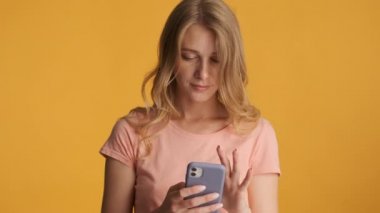 Çekici sarışın kız renkli arka planda kamerada akıllı telefon kullanıyor.