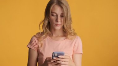 Güzel sarışın kız renkli arka planda kamerada akıllı telefon kullanıyor.