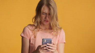 Dudak ısıran çekici sarışın kız ne yazık ki renkli arka planda akıllı telefonu kullanıyor. İfadeyi boz