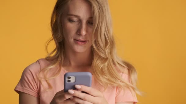 年轻而浓密的金发女子在彩色背景下 在相机上专注地使用智能手机 — 图库视频影像