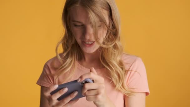 迷人而兴奋的金发女孩在色彩艳丽的背景下 通过智能手机在游戏中进行情感游戏 — 图库视频影像