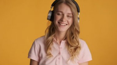Güzel sarışın kız rengarenk arka planda kulaklıkla müzik dinlerken mutlu bir şekilde dans ediyor.