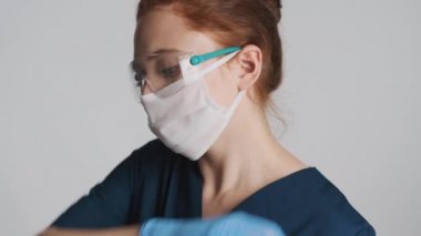 Koruyucu gözlüklü, maskeli ve tıbbi eldivenli kadın doktor omzunu kapatmış öksürüyor.